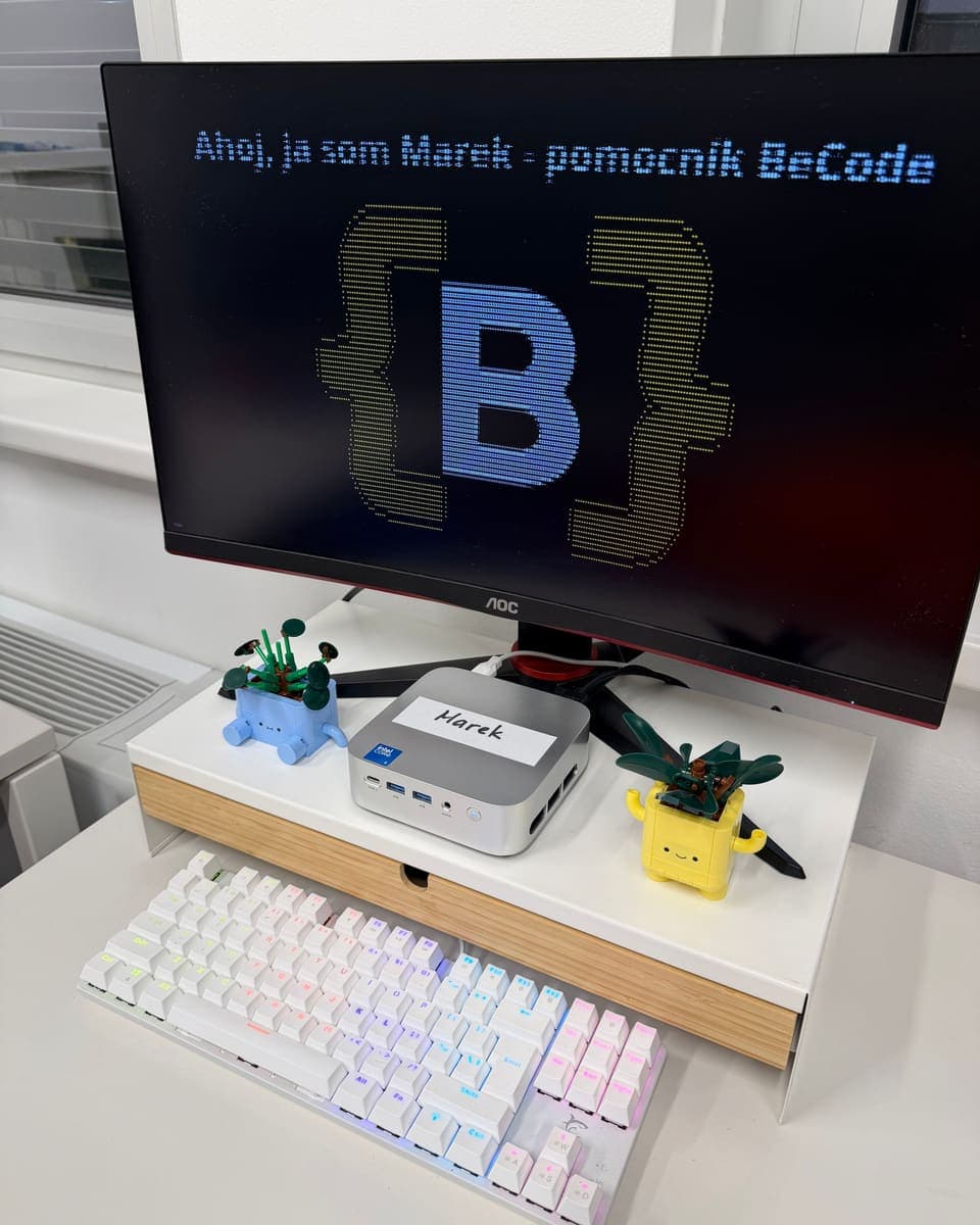 Marek in unserem Büro: ein silberner Mini-PC mit dem Namensschild „Marek“ unter einem Monitor mit dem Gruß „Ahoj, ja som Marek – pomocník BeCode“ (Hallo, ich bin Marek, der Helfer von BeCode)